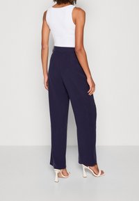 Marineblauwe wide-leg broek met een gladde textuur en een hoge tailleband. Gecombineerd met beige hoge hak sandalen. Minimalistisch wit tanktop.