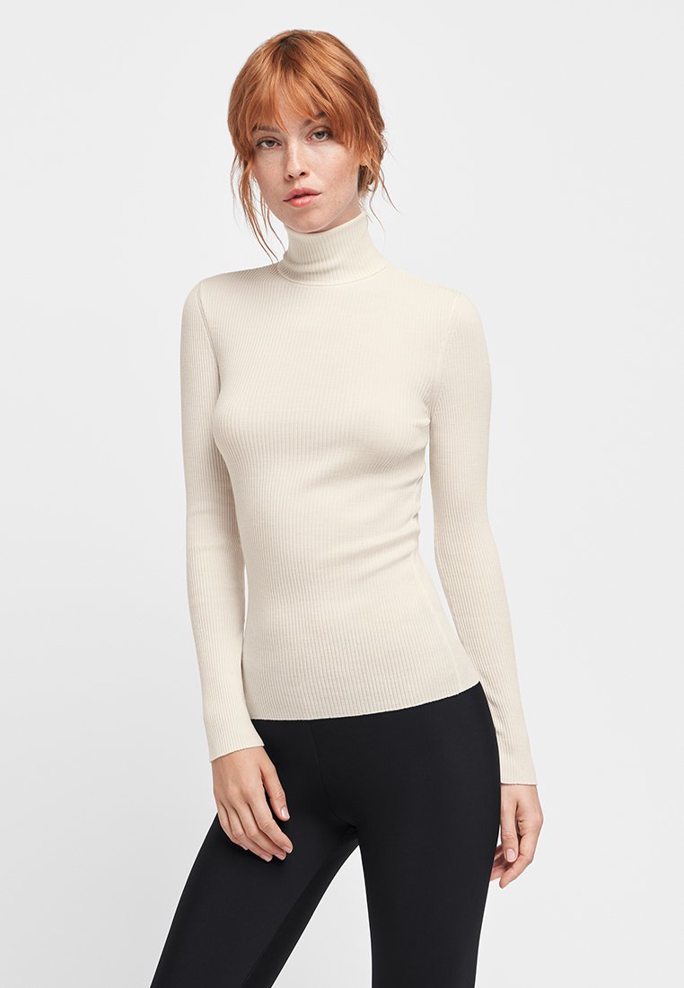 Ribbet, langærmet turtleneck-top i crème farve, tætsiddende design, blød tekstur, med høj hals og sømløs finish.