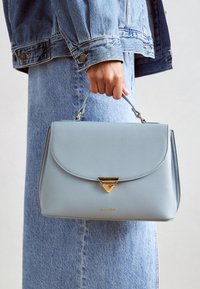 Bolso de mano de cuero azul claro con un clasp dorado en forma de triángulo. Presenta una forma estructurada, un asa superior y una textura suave. Logotipo en la parte frontal.