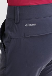 Pantaloni Columbia blu navy con una texture liscia, dotati di una cintura ampia e una tasca posteriore. Branding sottile sul lato.
