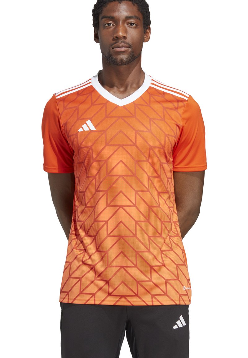 Maillot de sport orange avec un motif géométrique, comportant des accents blancs, un col en V et des manches courtes. Fabriqué en tissu respirant.