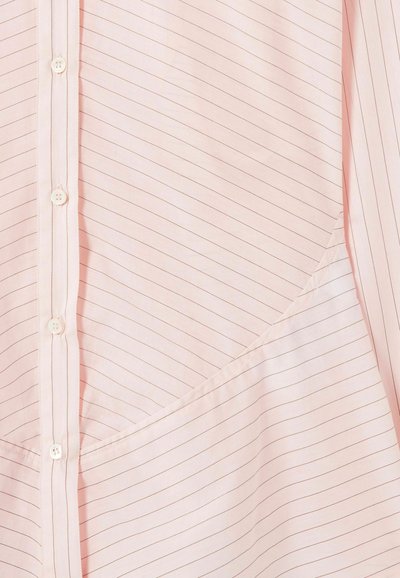 Camisa rosa claro abotonada con finas rayas diagonales y detalle de costura visible cerca del borde inferior.