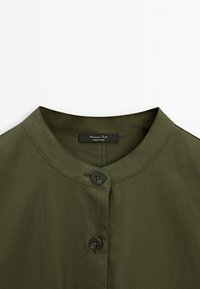 Chemise vert olive avec col rond et deux boutons visibles, affichant une étiquette de marque à l'intérieur portant le nom "Massimo Dutti".