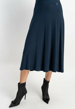 Marineblaue Midirock aus glattem Material mit schwingendem Saum und silbernem Akzent. Getragen mit schwarzen, hochhackigen Stiefeletten mit spitzen Zehen.