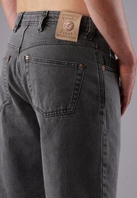 Close-up of back of person wearing gray jeans with patch label "Picaldi Jeans Authentic Design" on waistband.