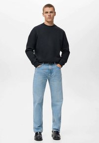 Zwarte crewneck sweatshirt, lichtblauwe rechte spijkerbroek en zwarte schoenen. Eenvoudig ontwerp zonder zichtbare patronen of grafische elementen.