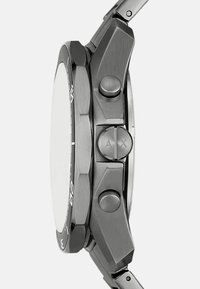 Plieninė laikrodžio korpusas su apvalia forma, ryškiu juodu disku ženklams, dviem mygtukais ir tekstūruotu pilku dėklu. Lygus paviršius su moderniu dizainu.