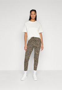 T-shirt blanche surdimensionnée à manches courtes, associée à des leggings à imprimé léopard. Le mannequin porte des baskets blanches et des chaussettes blanches à la cheville.