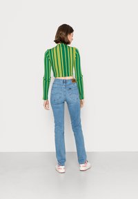Top a maniche lunghe cropped a righe verdi e gialle abbinato a jeans blu chiaro. Presenta il marchio Lee sulla tasca posteriore e sneaker bianche.
