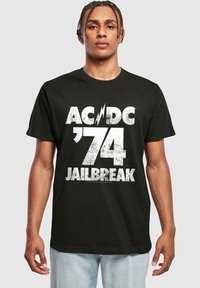 Sort bomulds T-shirt med en stor, slidte hvid grafisk tryk med "AC/DC ’74 JAILBREAK" i fed skrift. Korte ærmer, afslappet pasform.