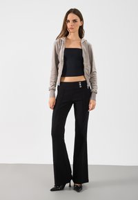 Γκρι βελούδινο φούτερ με φερμουάρ, μαύρο crop top και μαύρο καμπάνα παντελόνι με τρία ασημένια κουμπιά στη μέση, και μαύρες μυτερές γόβες.