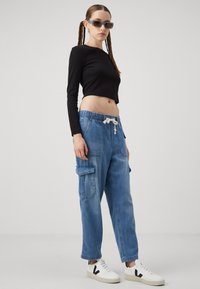 Svart kortärmad topp med lång ärm, blå denim cargo-byxor med elastisk midja och fickor, vita sneakers med svarta detaljer och snörningar.