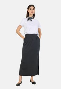T-shirt bianco, gonna maxi nera con spacco laterale, indossata con una sciarpa stampata e scarpe flat. Il tessuto appare liscio e cade in modo elegante.