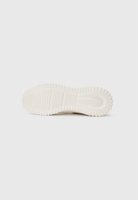 White sneaker sole with deep grooves and ridges for traction, featuring "Calvin Klein Jeans" text embossed near the heel.
