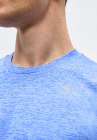 Κοντινό πλάνο στον λαιμό και το σαγόνι ενός ατόμου που φοράει ένα αθλητικό μπλουζάκι ανοιχτού μπλε χρώματος με μικρό λευκό λογότυπο στο στήθος.