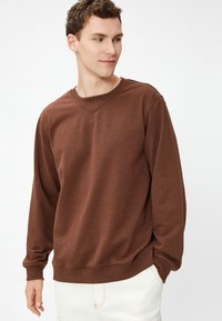 Brązowy sweter z dekoltem w serek, długimi rękawami i ściągaczami. Wykonany z miękkiego materiału; posiada luźny krój i gładką fakturę.