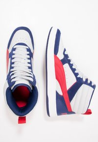 Vysoké tenisky s šedou koženou a námořnickou semišovou svrškem, červenými akcenty, bílou gumovou podrážkou a šněrováním. Odolná textilní podšívka.