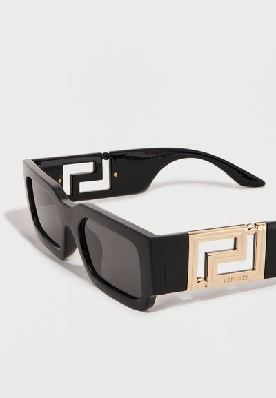Μαύρα ορθογώνια γυαλιά ηλίου με χρυσές γεωμετρικές λεπτομέρειες στους βραχίονες και σκουρόχρωμους φακούς.
