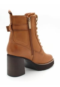 Skórzane botki za kostkę w kolorze brązowym, na obcasie blokowym, z bocznym zamkiem błyskawicznym, sznurowanym przodem i uchwytem do zakupu na gładkim białym tle.