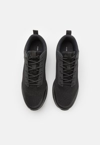 Black athletic shoes with a textured fabric upper, thin laces, and a supportive sole. Features a pull tab at the heel for easy wear.