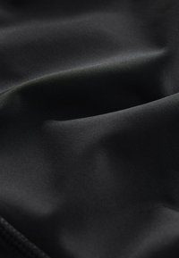 Tissu extensible noir au toucher lisse, affichant un léger éclat et des courbes douces, indiquant douceur et malléabilité.