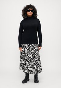 Svarte turtleneck-genseren er kombinert med et langt, flytende skjørt i svart og hvitt med abstrakt mønster og svarte ankelstøvler.