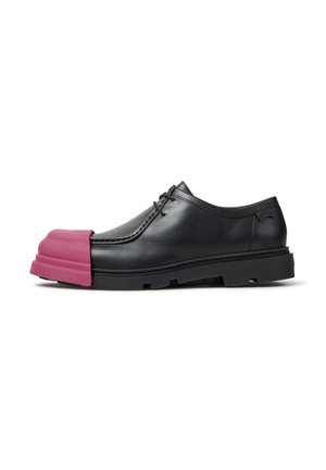 Zwarte leren veterschoen met dikke zool en een overdreven roze rubberen teenkap die aan de voorkant uitsteekt.