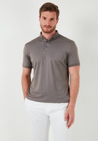 Šedé polo tričko s špičatým límcem, dvěma knoflíky, krátkými rukávy a hladkým materiálem. Nosené s bílými kalhotami pro kontrast.