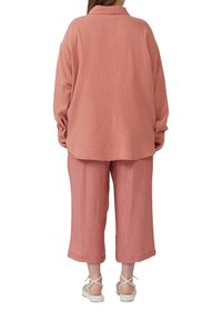 Chemise en coton texturé rose à coupe ample, associée à un pantalon court assorti. Elle possède un col et des manches longues. Portée avec des sandales blanches à lanières.