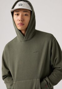 Φούτερ με κουκούλα σε ελιά πράσινο χρώμα, με τσέπη καγκουρό και κεντημένο λογότυπο Levi's. Διαθέτει απαλό βαμβακερό υλικό και άνετη εφαρμογή.