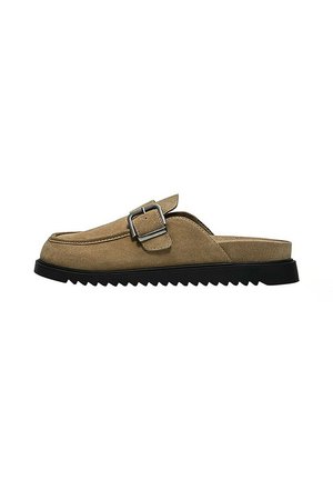 Chaussure en daim marron à enfiler avec semelle noire dentelée et boucle argentée sur le dessus, vue de côté sur fond blanc.