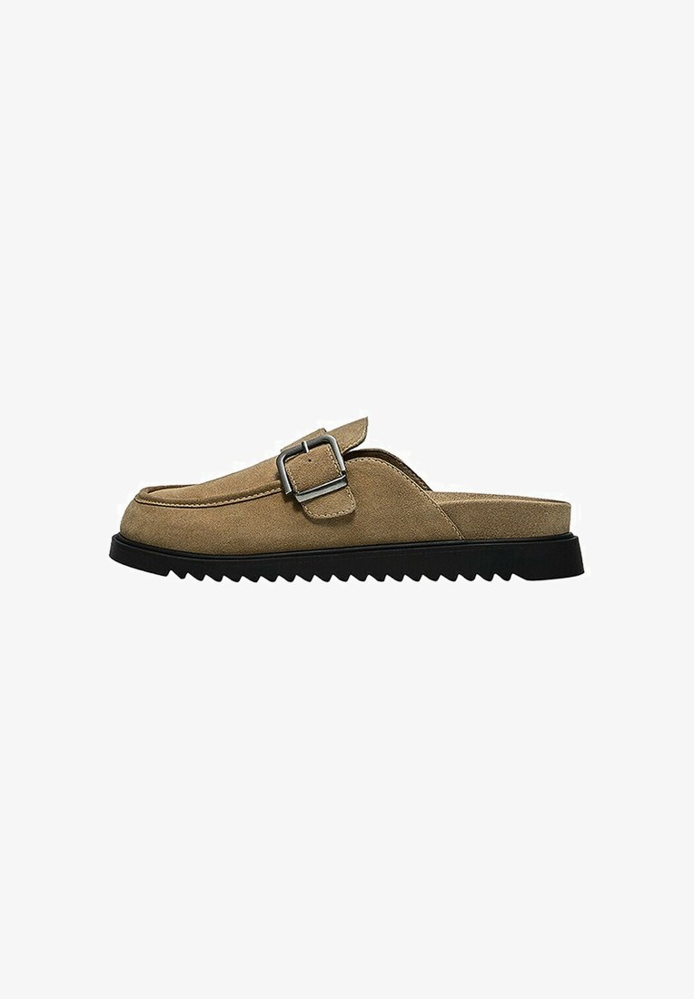 Chaussure en daim marron à enfiler avec semelle noire dentelée et boucle argentée sur le dessus, vue de côté sur fond blanc.
