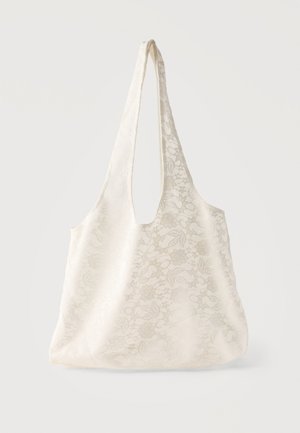 White fabric tote bag with floral lace pattern and wide handles hanging against plain background.