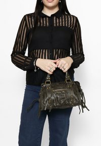 Zwarte transparante blouse met gestreept patroon en knoopsluiting, gecombineerd met een kleine grijze leren handtas met studs, ritsen en franjes.