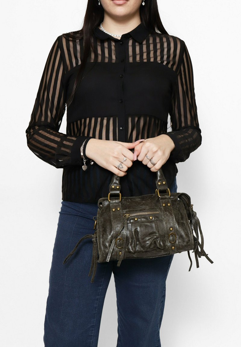 Zwarte transparante blouse met gestreept patroon en knoopsluiting, gecombineerd met een kleine grijze leren handtas met studs, ritsen en franjes.