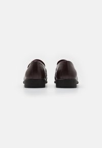 Chaussures en cuir marron avec une finition lisse, bout arrondi, petit talon noir et détails de couture subtils à l'arrière.