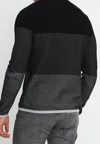 Maglione lavorato a maglia con design a blocchi di colore in nero e grigio, caratterizzato da una scollatura rotonda e tessuto testurizzato sulla schiena e sulle maniche.