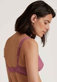 Reggiseno in pizzo color malva con spalline regolabili. Presenta un motivo floreale, una consistenza morbida e una chiusura con gancio e occhiello sul retro.