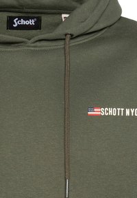 Olivgrüner Kapuzenpullover mit Kordelzug, versehen mit einem sichtbaren Logopatch und einem Design der amerikanischen Flagge. Weicher Stoff mit glatter Textur.