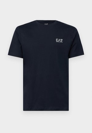 Camiseta de algodão azul marinho com mangas curtas, gola redonda e um pequeno logótipo branco bordado no lado esquerdo do peito. Textura suave.
