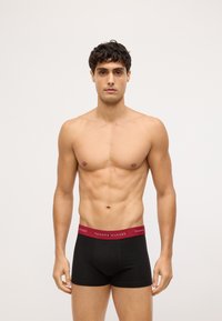 Boxer briefs negros con una cinturilla burdeos que presenta el logo "TOMMY HILFIGER". Tela suave, diseño ajustado y corte de altura media.