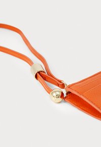 Orange leather pouch with a textured finish, featuring a gold-toned hardware accent and adjustable strap. Zipper closure detail visible.