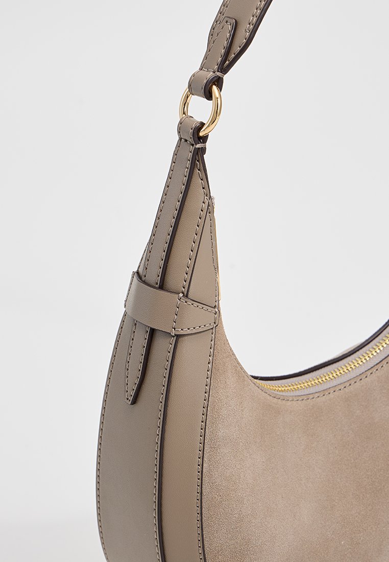 Beige leren tas met een gladde en suède textuur, voorzien van gouden hardware en een gebogen ontwerp. Inclusief een gestructureerde schouderriem.