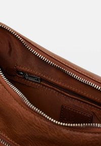 Braune Ledertasche im Inneren, mit glatter Textur, einer Reißverschlusstasche und einem silbernen Reißverschlussrand. Braune Stoffauskleidung sichtbar im Inneren.