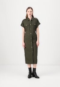 Rochie verde măsliniu, cu butoniera, mâneci scurte, două buzunare frontale și croială dreaptă, asortată cu cizme negre până la gleznă.