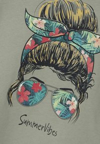 Camiseta verde con un diseño impreso de un peinado en moño, gafas de sol con un patrón tropical y el texto "SummerVibes" debajo.
