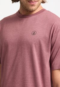 Camiseta de manga corta en color maroon, hecha de una mezcla de algodón, con un pequeño logo negro en el pecho y un clásico cuello redondo.