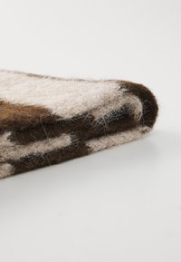 Bruin en crème viltwol stof, gevouwen met een zachte textuur, met een gespikkeld patroon. De randen zijn lichtjes rafelig, wat detail toevoegt.