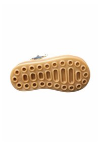Suola di scarpa in materiale gommoso marrone chiaro e testurizzato. Presenta ritagli circolari e ovali per trazione e flessibilità.