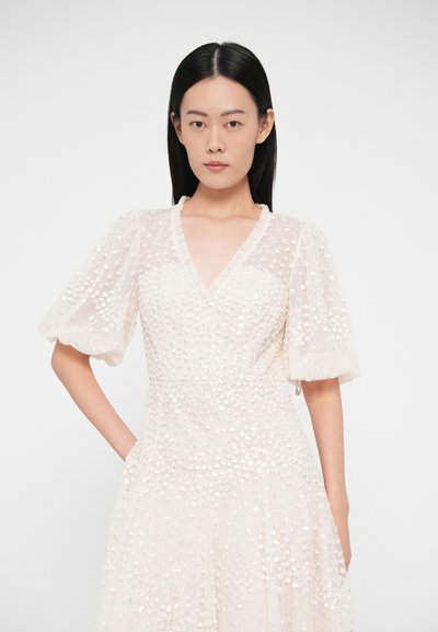 Φόρεμα σε ανοιχτό κρεμ χρώμα με ντεκολτέ σε σχήμα V, κοντά φουσκωτά μανίκια, υφασμένο ύφασμα με μικρές, λαμπερές λεπτομέρειες παντού. Αέρινη σιλουέτα.